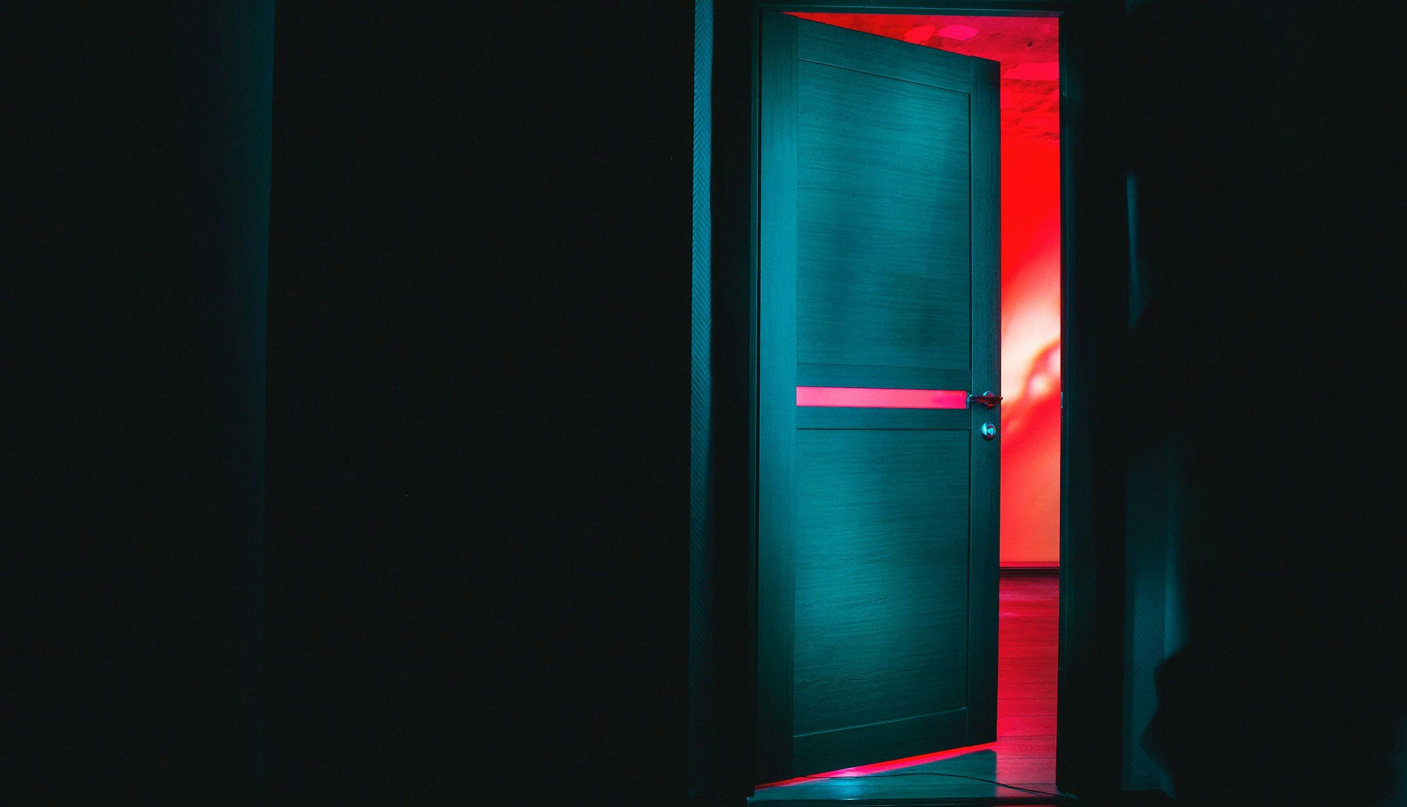 Bilde av dør som går fra mørkt rom til rom med rødt lys.