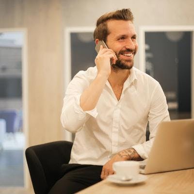 Smilende mann sitter på kontor og snakker i telefonen.