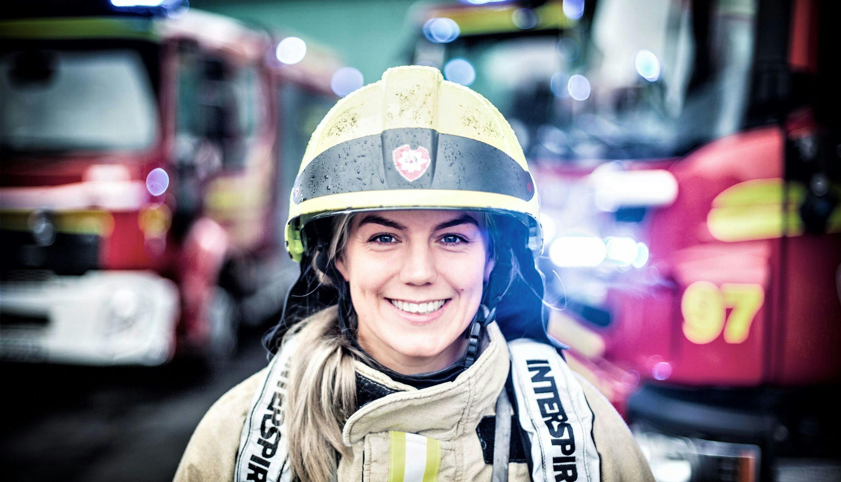 Portrett av Lise Sirnes Aspenes i brannutstyr foran brannbiler.