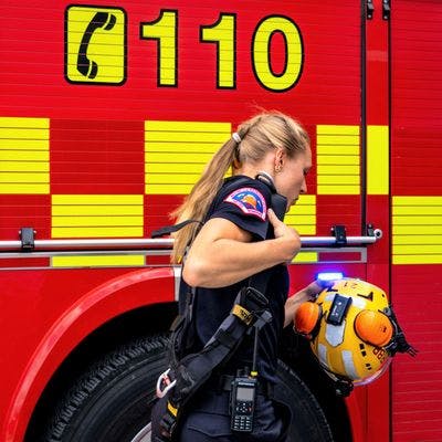 Kvinnelig brannkonstabel holder en hjelm mens hun går forbi en brannbil.