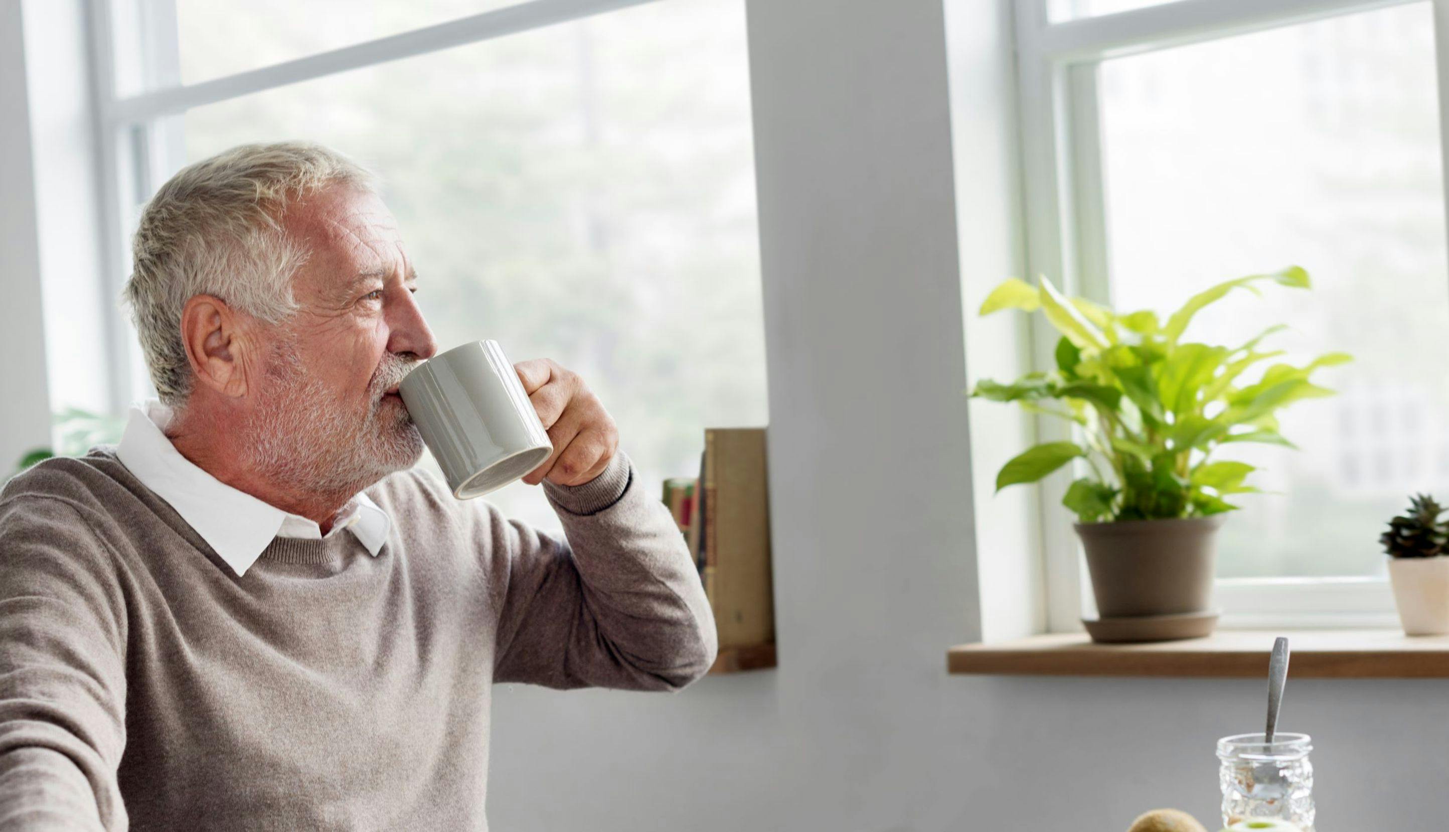Eldre mann drikker kaffe og ser ut av vinudet. 