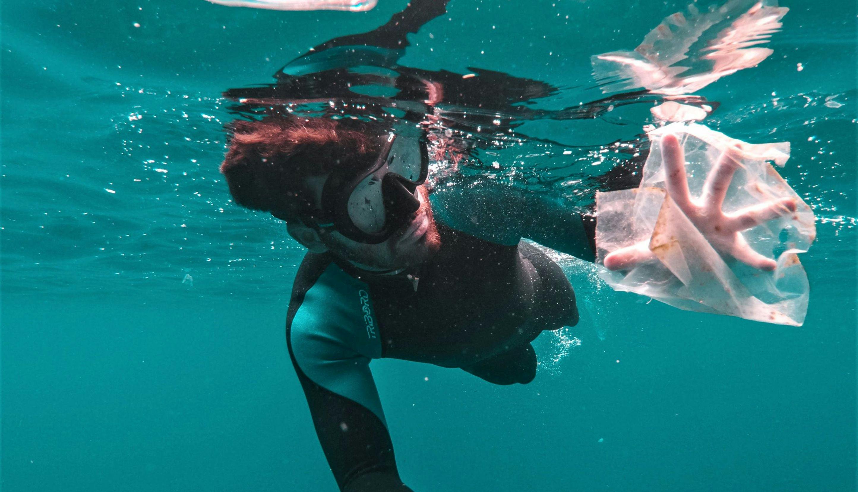 Dykker som samler plast under vann.