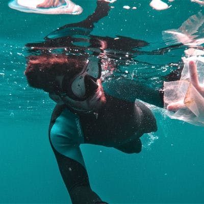 Dykker som samler plast under vann.