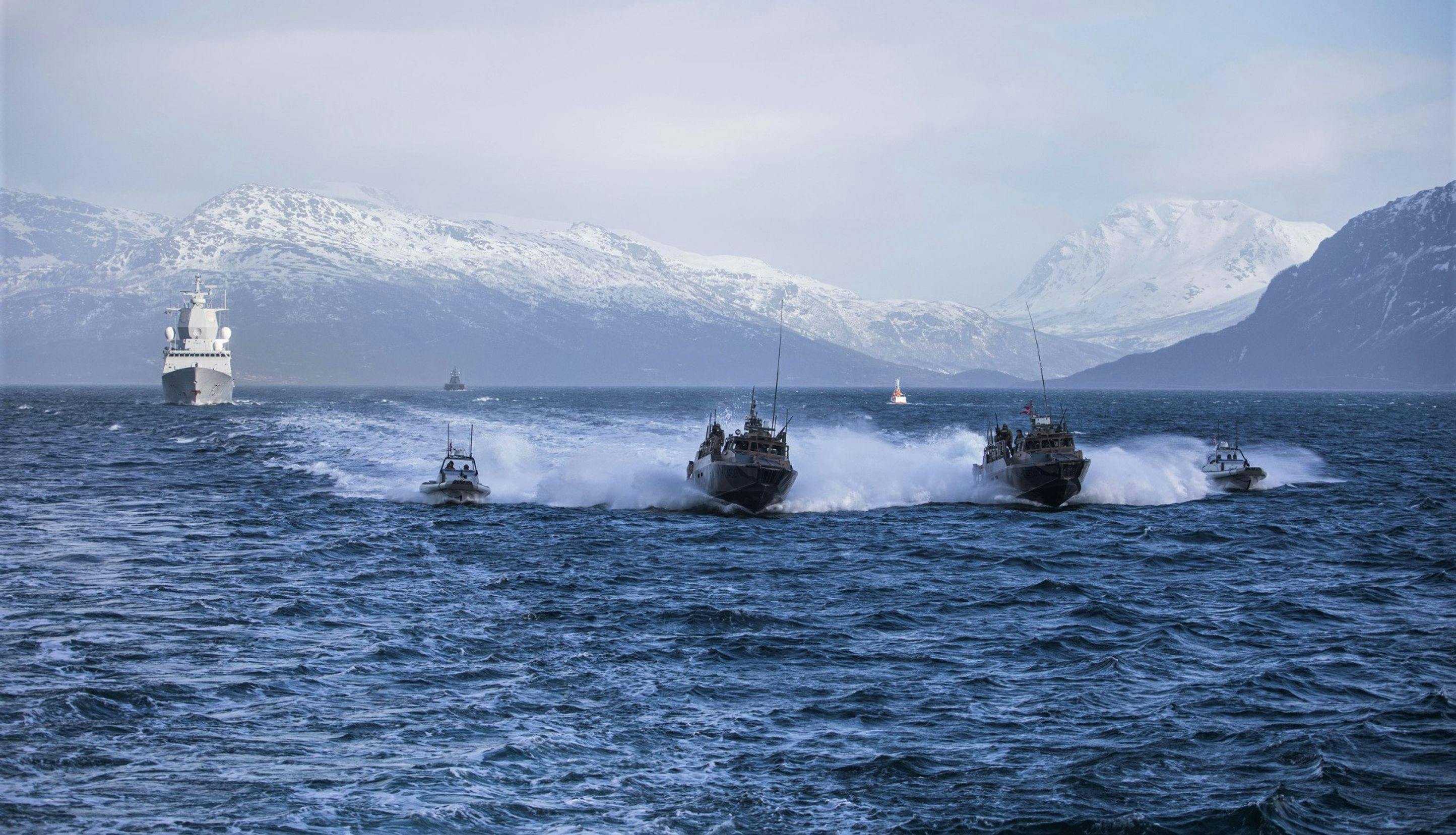 En fregatt, to stridsbåter og to lettbåter, alle fra Den norske marinen, fosser frem i en fjord.