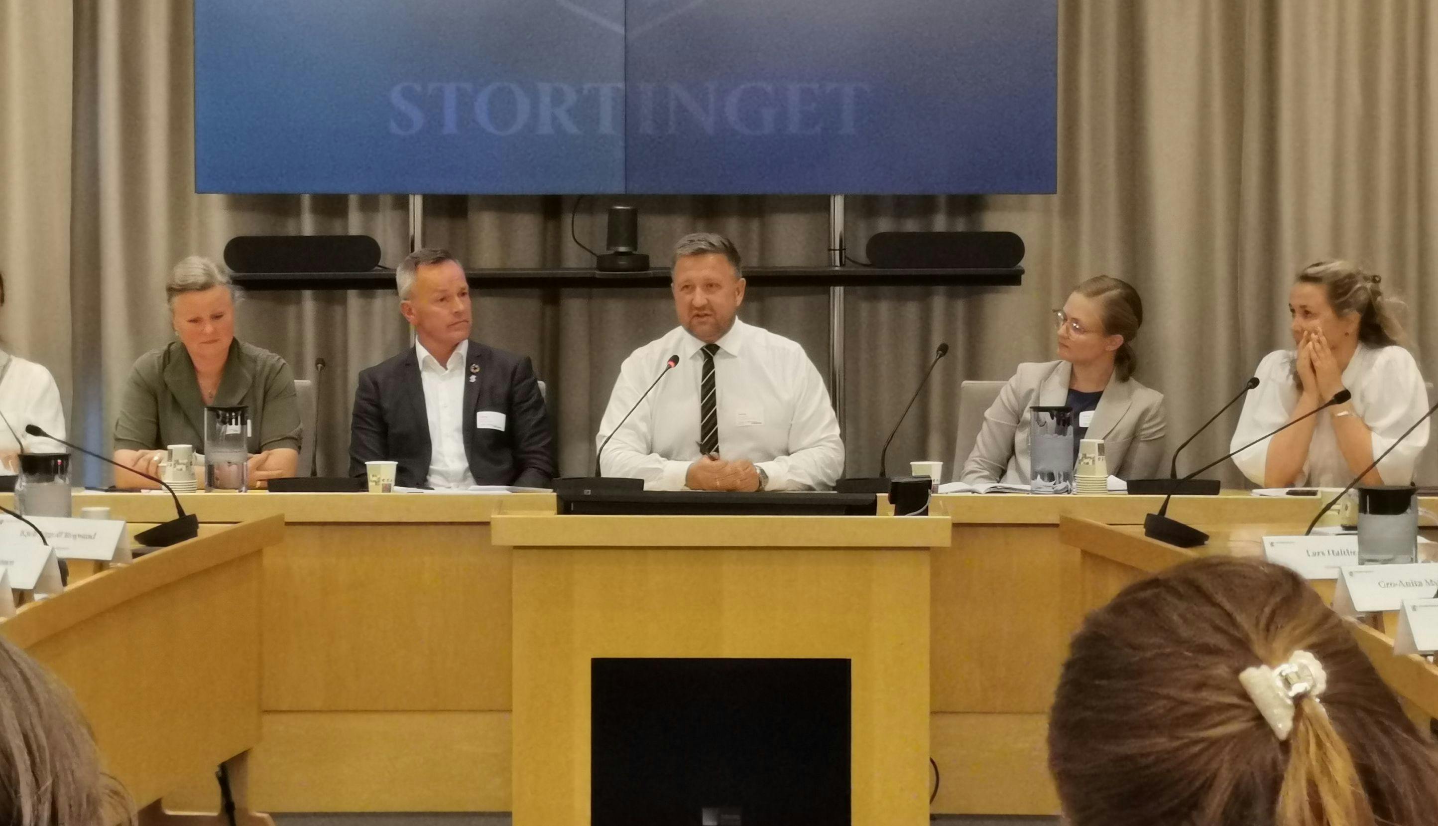 Truls Wickholm, Øivind Brevik og Pia Farstad von Hall sitter ved bord i høring i Stortinget.