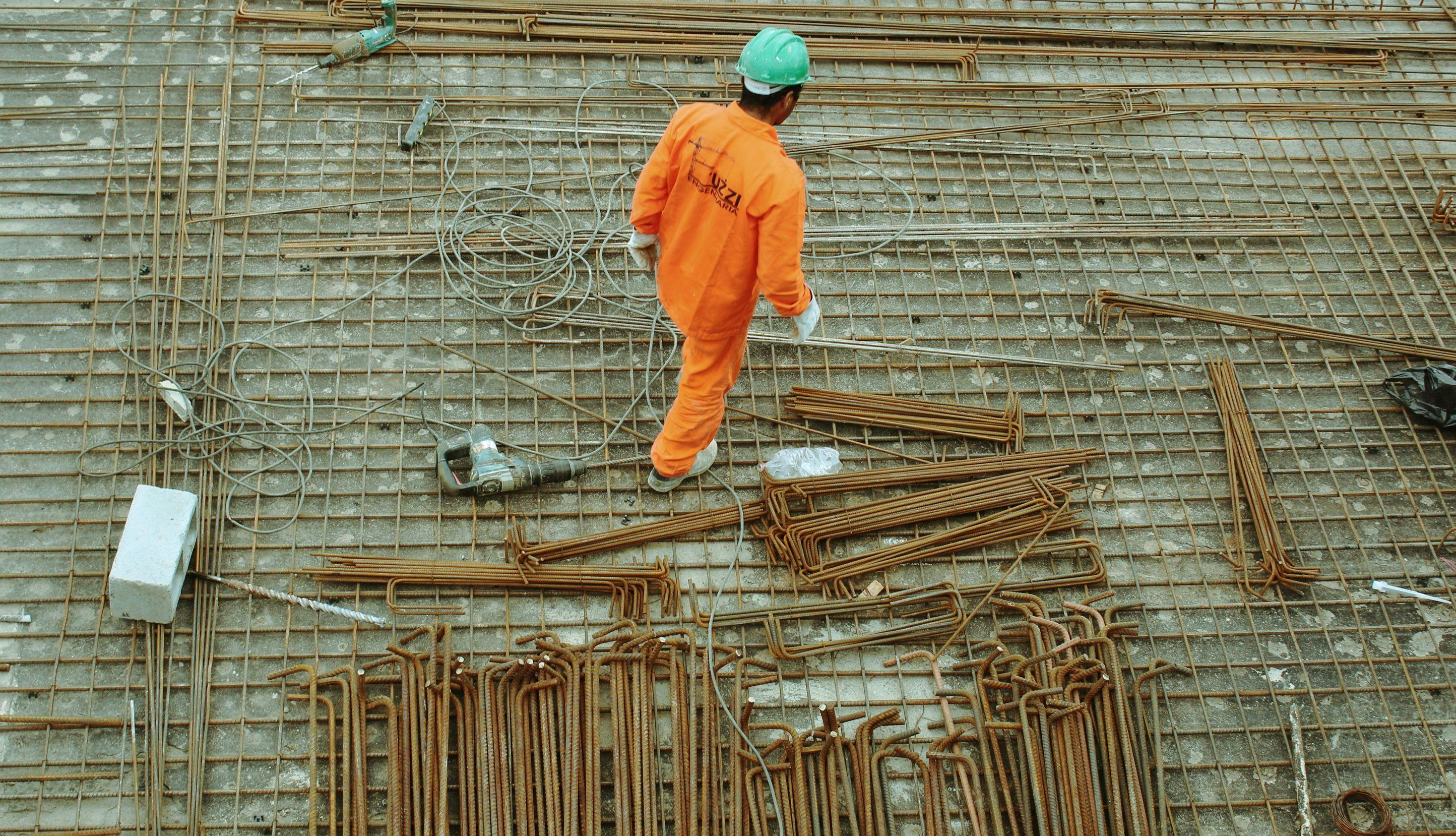 Arbeider med hjelm og oransje arbeidsdrakt går rundt på en byggeplass. 