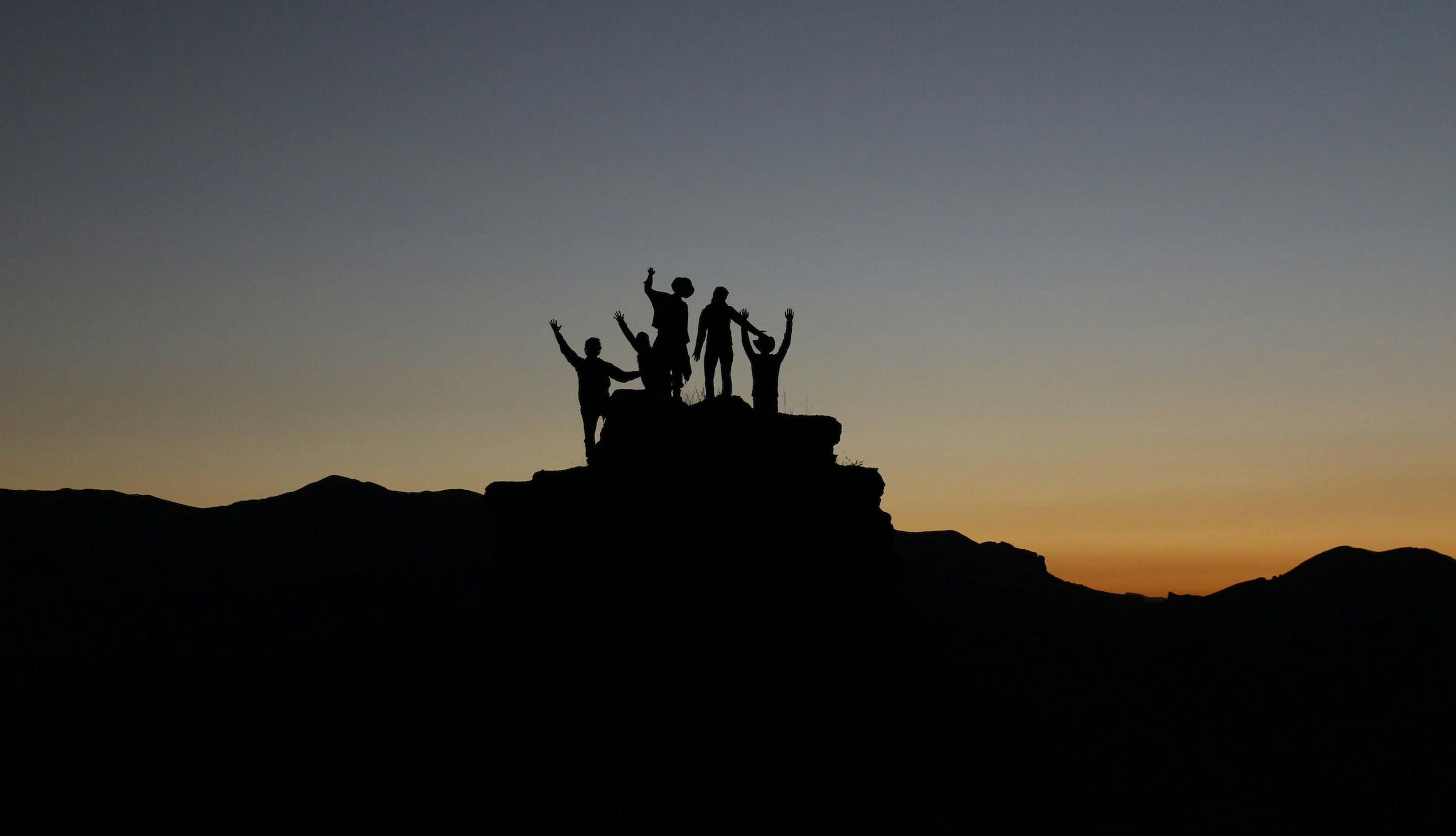 Gruppe mennesker som står på en topp i solnedgang.