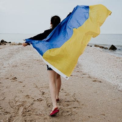 En ung kvinne går langs stranden ved Azovhavet og holder et ukrainsk flagg som blafrer i vinden.