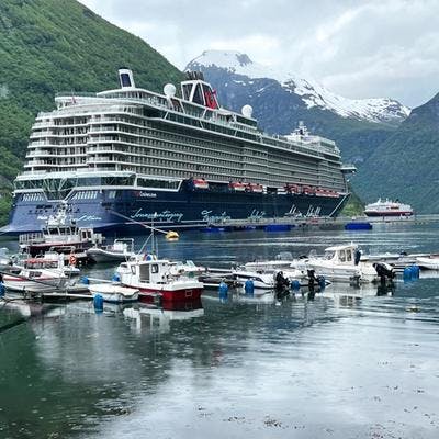 Cruiseskip ligger til kai i en fjord med snødekte fjelltopper i bakgrunnen. 
