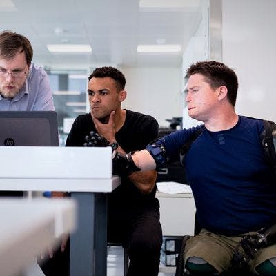 Tre personer som ser på dataskjerm. hvor den ene har proteser.
