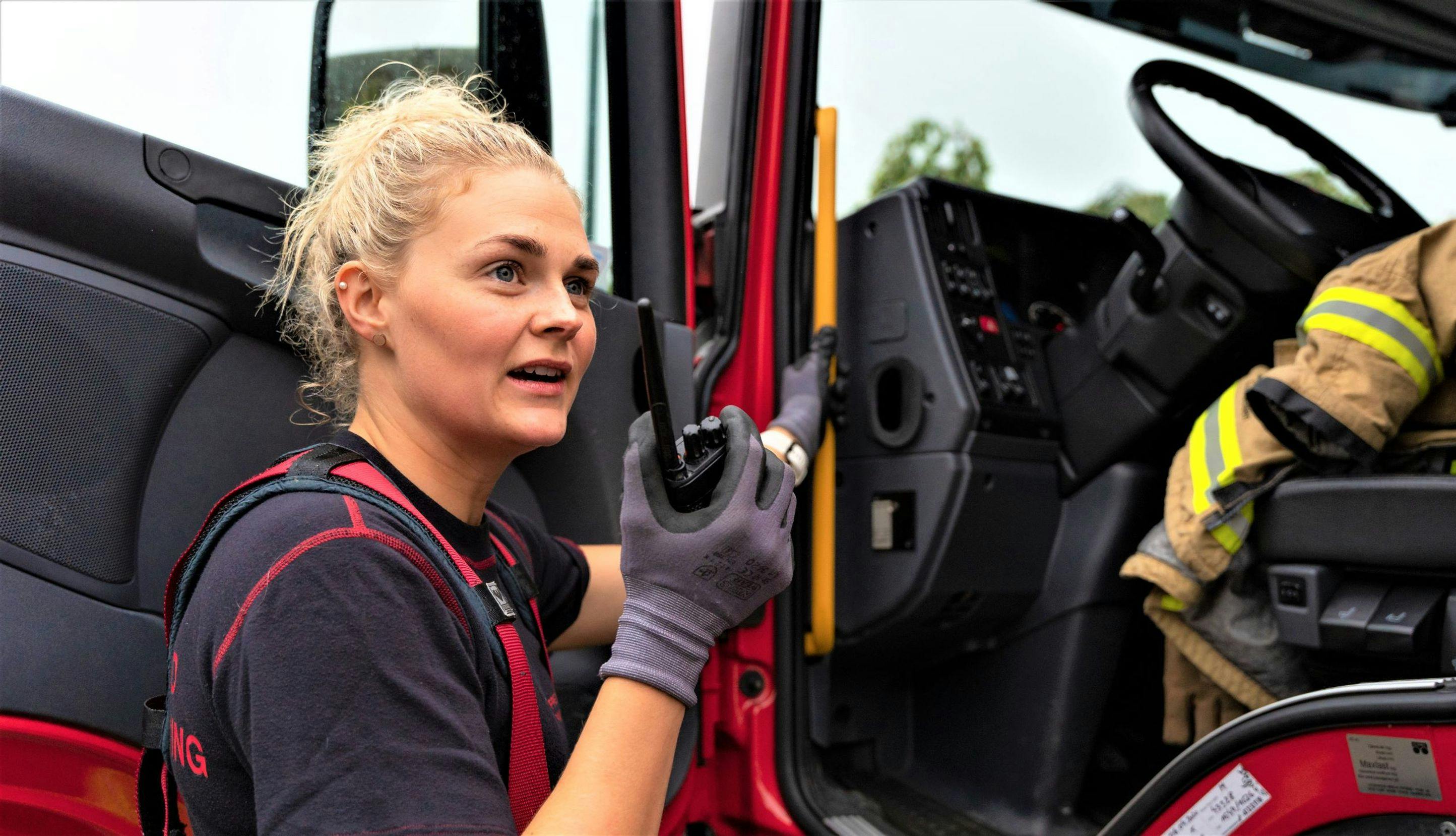 Kvinnelig brannkonstabel snakker i walkie-talkie utenfor brannbil.