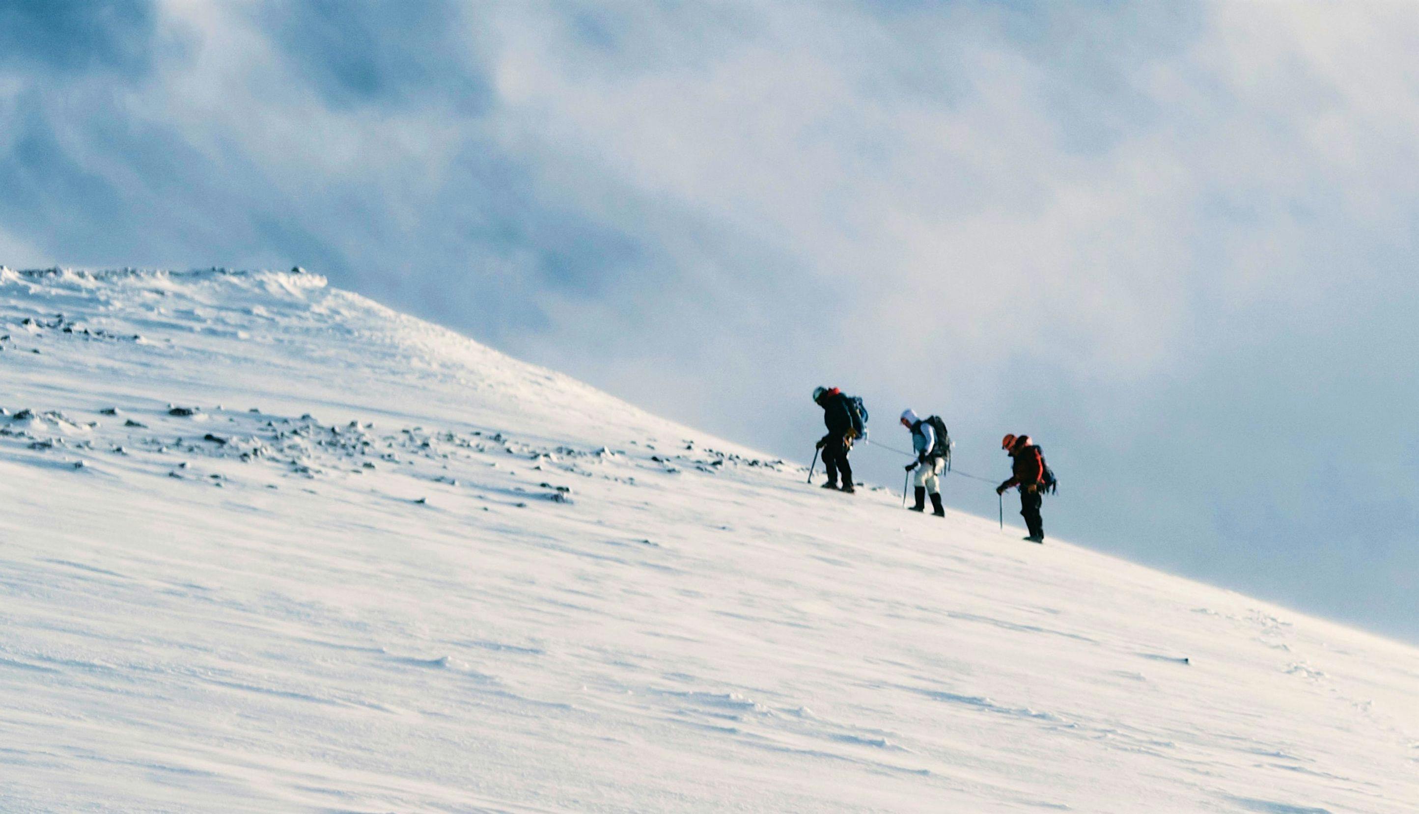 Tre fjellklatrere på vei opp et snødekt fjell.
