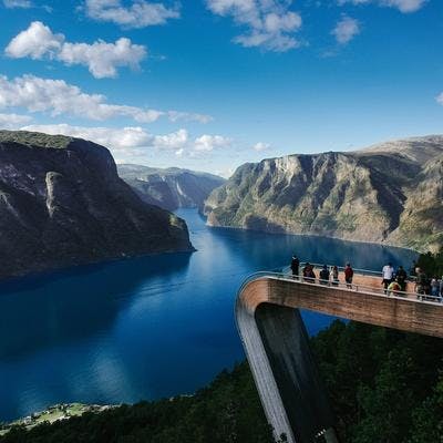 Folk står på et utsiktspunkt av tre og ser ut over en fjord. 